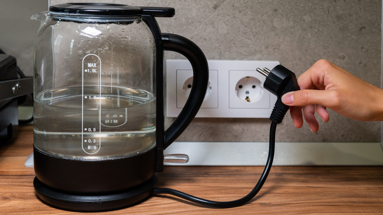 Unplugging electric kettle holding water on wooden counter