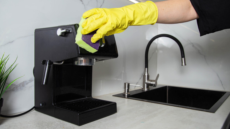 Gloved hand wiping black coffee machine with sponge