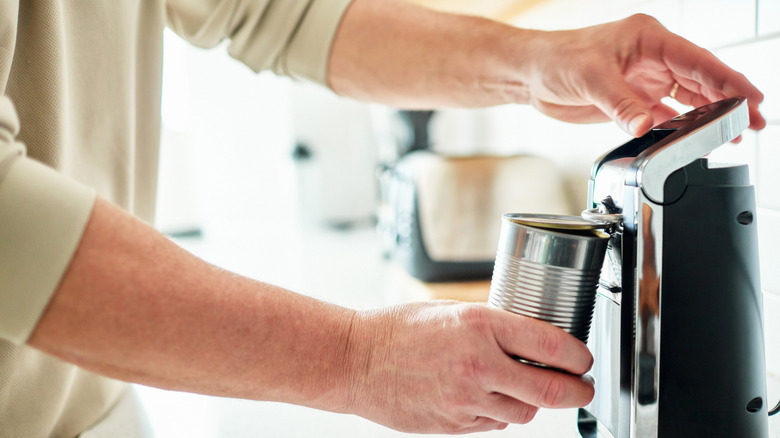 Hand using electric can opener to open tin can