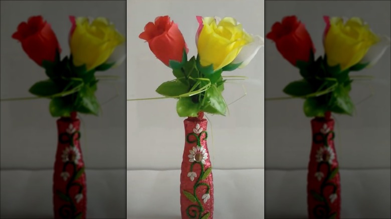 Plastic vinegar bottle repurposed into a glittery red flower vase with red, pink, white, and yellow flowers inside it.