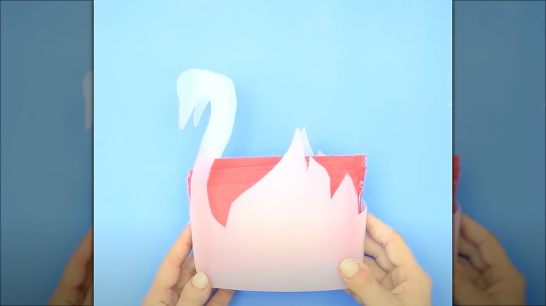 Person holding a plastic DIY napkin holder that is shaped like a swan.