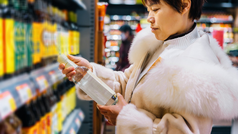 A person holding a glass vinegar bottle in the grocery store.