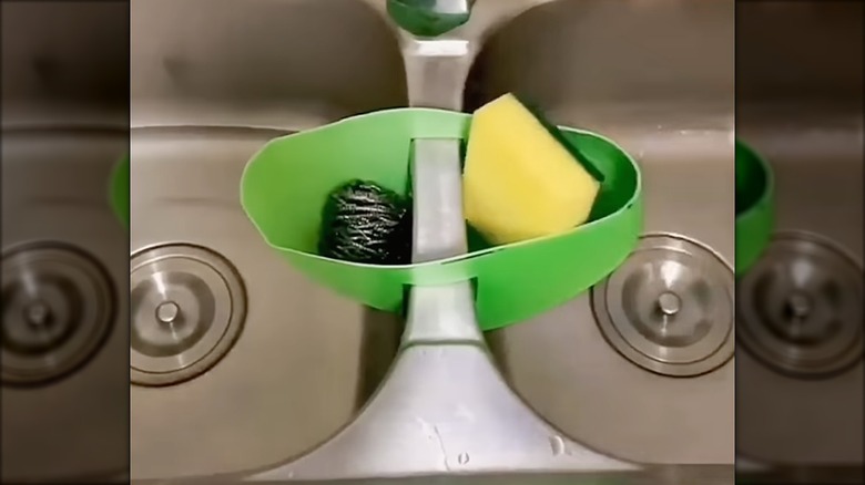 Green plastic sponge caddy resting in the middle of a two compartment sink.