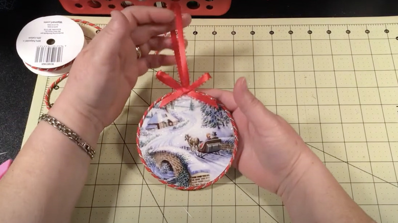 A woman holds a Christmas tree ornament made from coasters