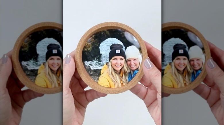 A woman holds up a photo hot glued inside a cork coaster.