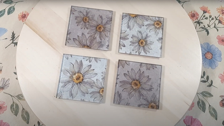 Old glass coasters have had floral tissue added to them using decoupage.