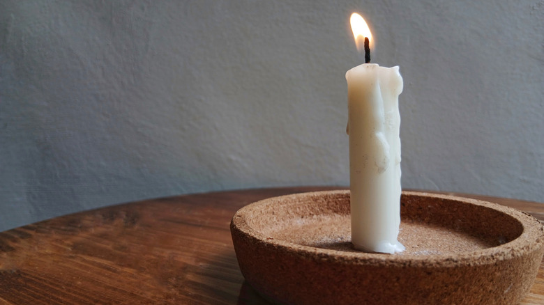 A burning white pillar candle sits on top of a cork drinks coaster.