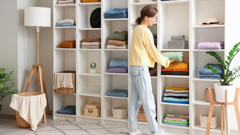 Woman putting folded sweater onto closet shelf