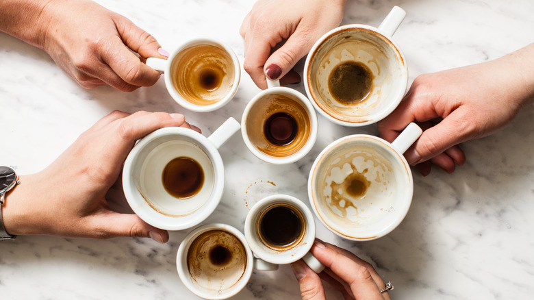 Hands holding stained coffee mugs