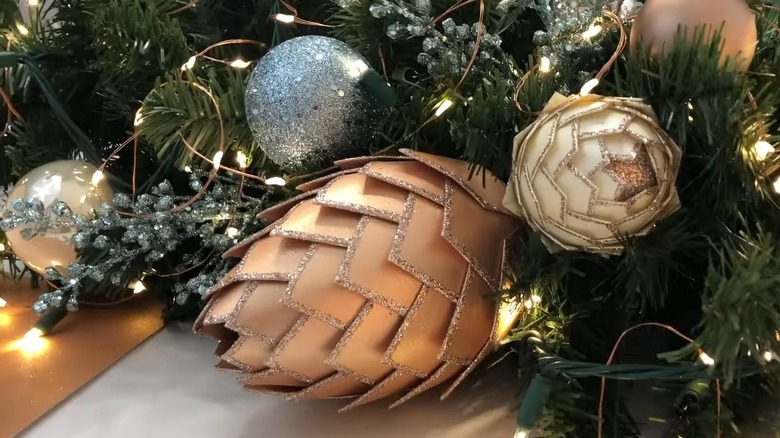 Cardstock pine cones near evergreen, glitter Christmas balls, and string lights