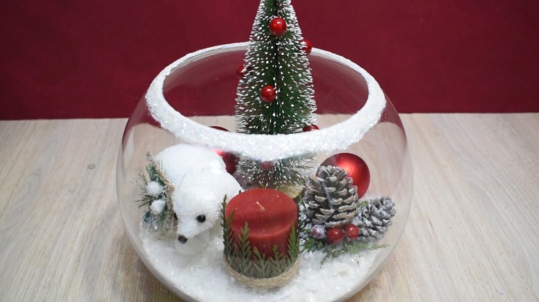 Christmas wonderland in a bowl containing candle, polar bear, pine cones, faux snow, and decorated conifer