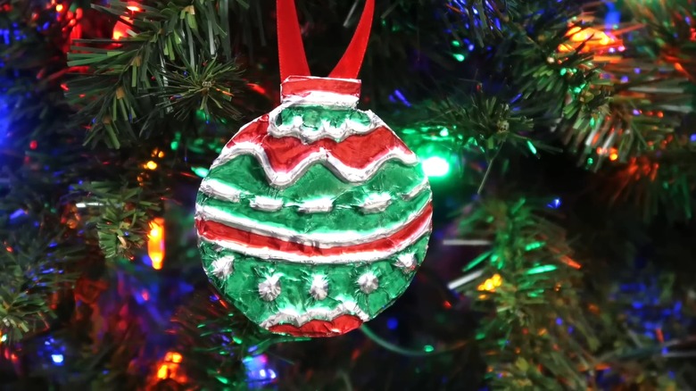 Foil paper Christmas ornament hanging from tree with a red ribbon