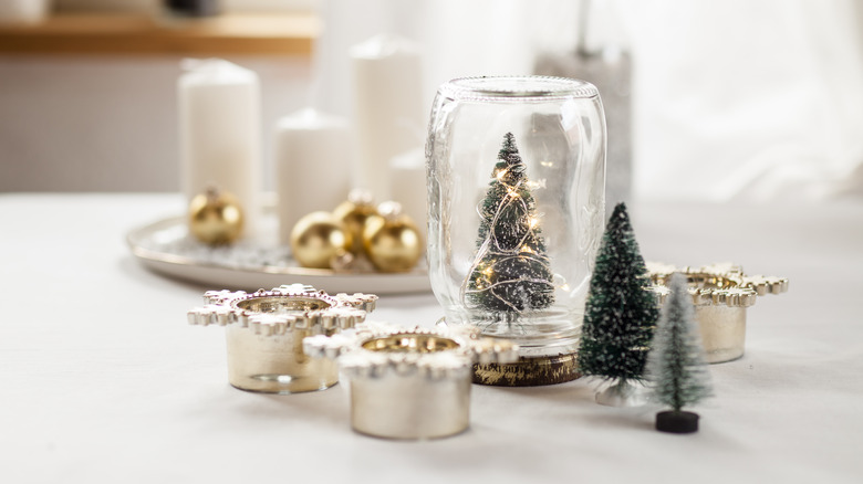 Conifer in glass jar with other Christmas decor on white table