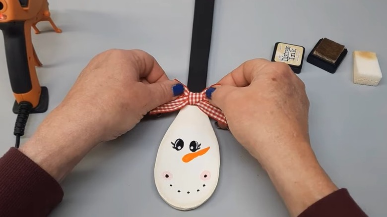 Adding ribbon to snowwoman on a wooden spoon