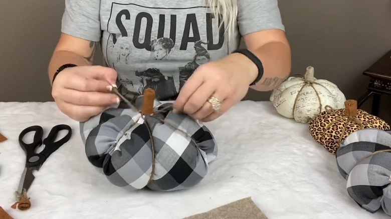 Person tying twine around plush pumpkin