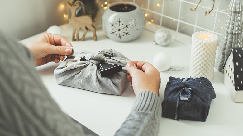 A person wrapping a present with a gray scarf