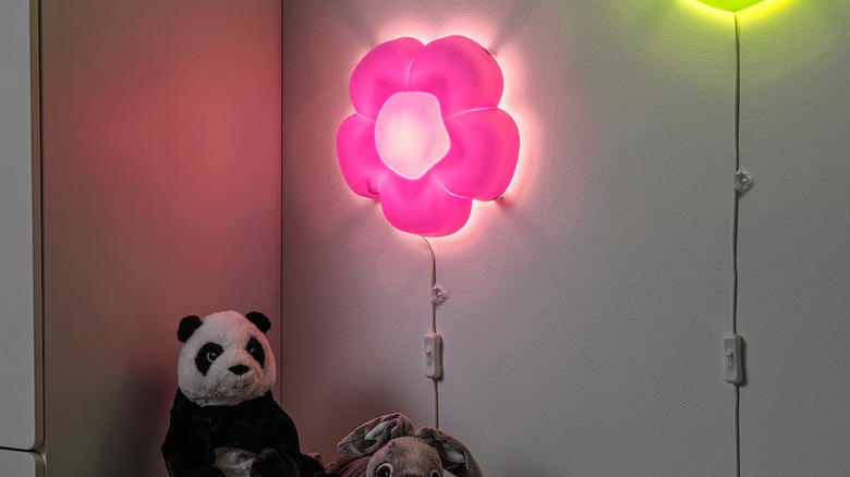 pink flower lamp on wall over shelf of stuffed animals