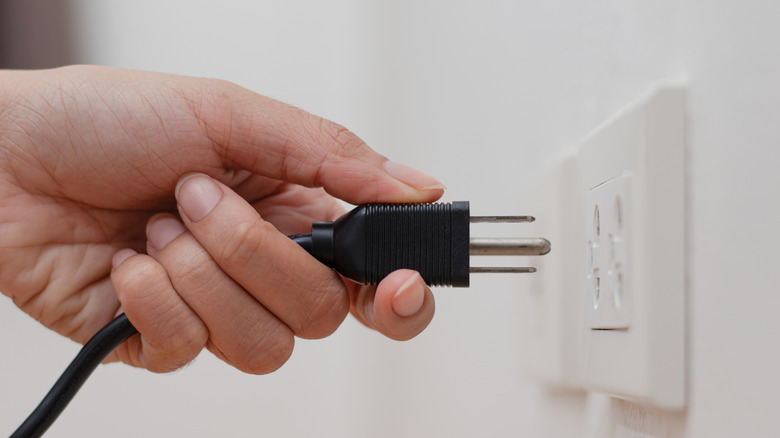 hand unplugging power cable form outlet