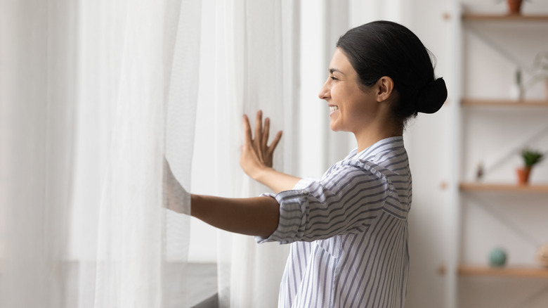 woman opening white curtains