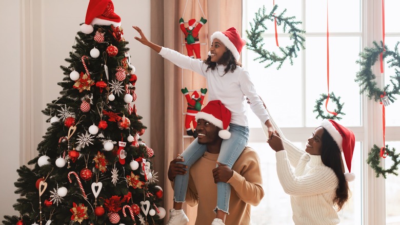 A family of three is decorating a Christmas tree