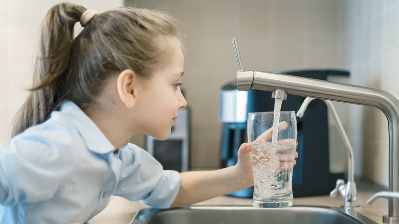 Girl holding glass under faucet