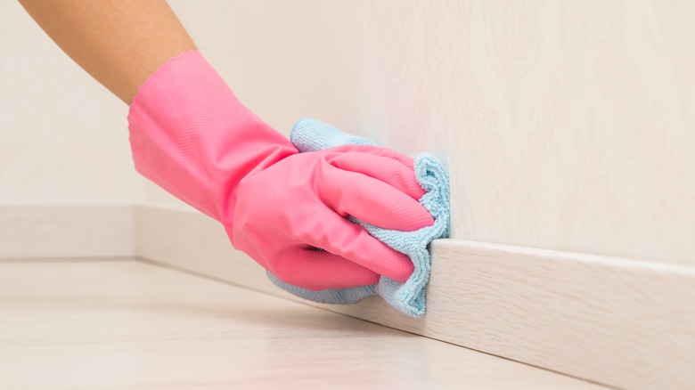 person cleaning baseboards with rag