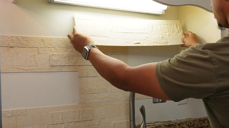 Man applies peel-and-stick stone panels to kitchen backsplash