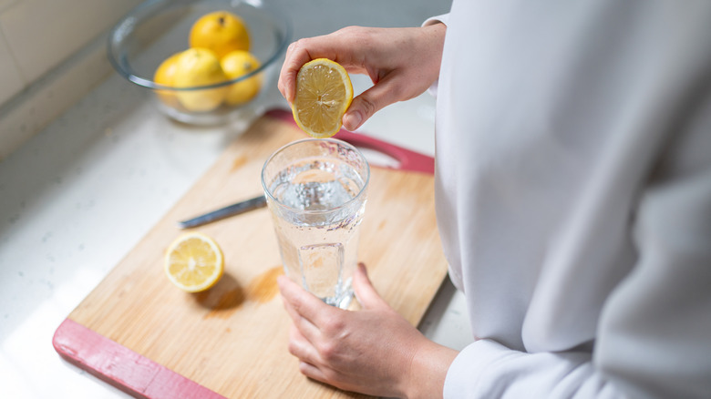 Woman Squeezing A Lemon Into A Glass Of Water