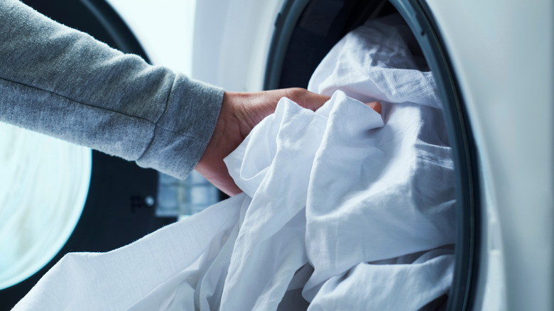 person putting sheets into washer