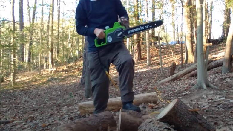 Man cutting logs with a corded Greenworks chainsaw