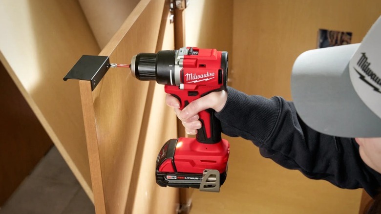 Man in Milwaukee hat drilling magnetic catch onto cabinet door with compact Milwaukee drill