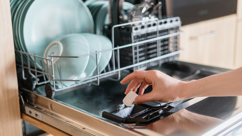 Hand of a person putting a dishwasher tablet into an open dishwasher