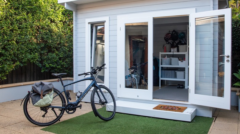 Blue bike with backpack in front of organized white shed with glass door