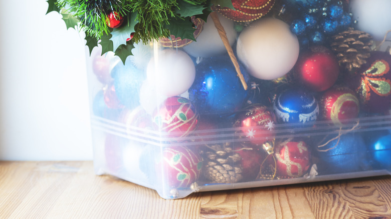 Blue, red, and white Christmas tree ornaments in clear plastic bin on wood floor