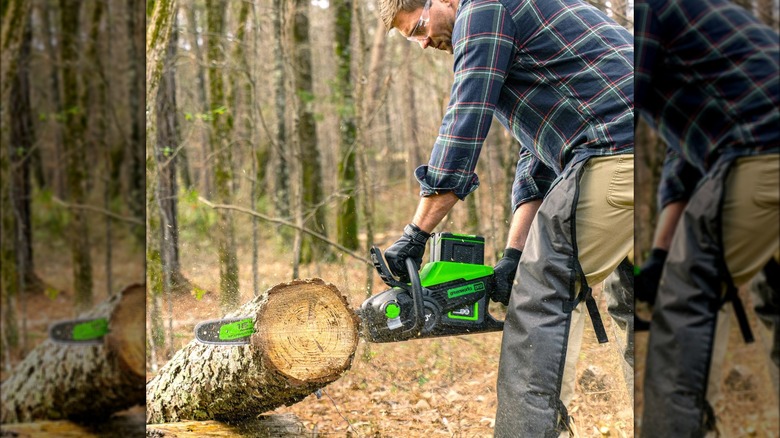 A man wearing a flannel shirt uses a Greenworks chainsaw to cut a log in the woods