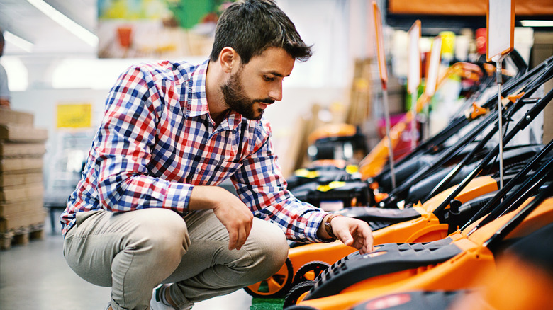 Man crouches down to look at lawn mowers