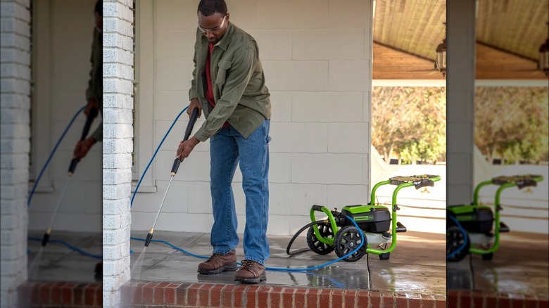 A man stands on a porch while using a Greenworks pressure washer to clean bricks