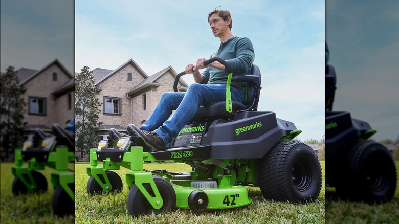 A man drives a Greenworks zero-turn lawnmower in front of his brick home