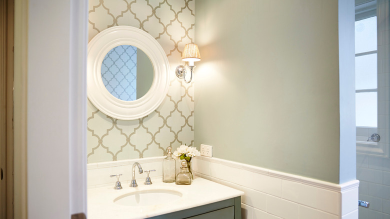 Round bathroom mirror with small sconce above vanity