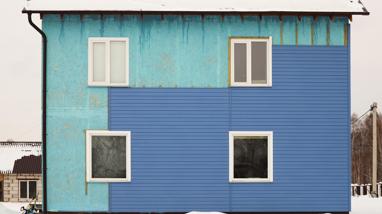 A house with half of its blue vinyl siding removed