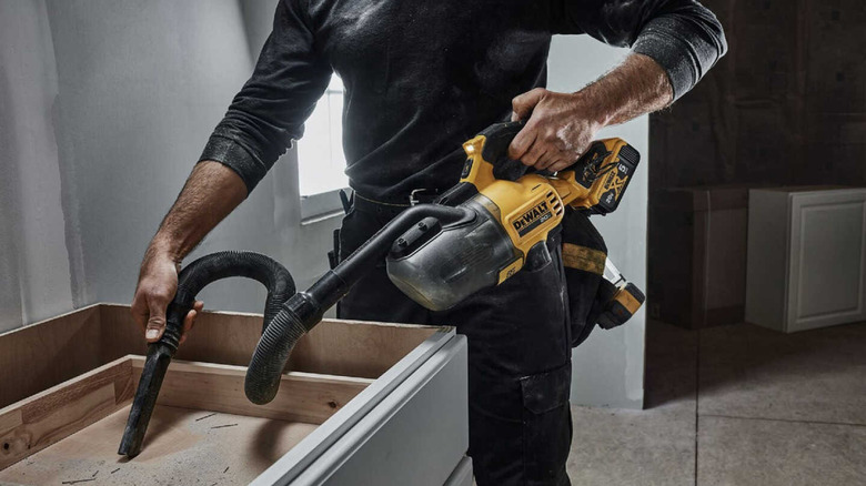 A man uses a cordless DeWalt handheld vacuum to clean dust out of a cabinet