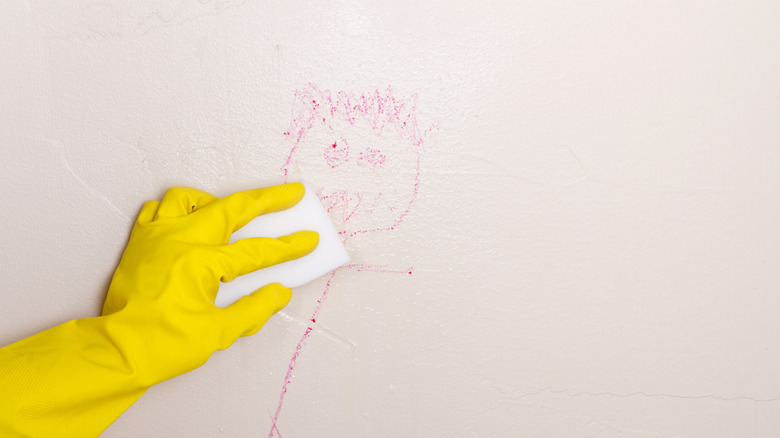 Person wearing a yellow glove to clean red crayon off a white wall with magic eraser