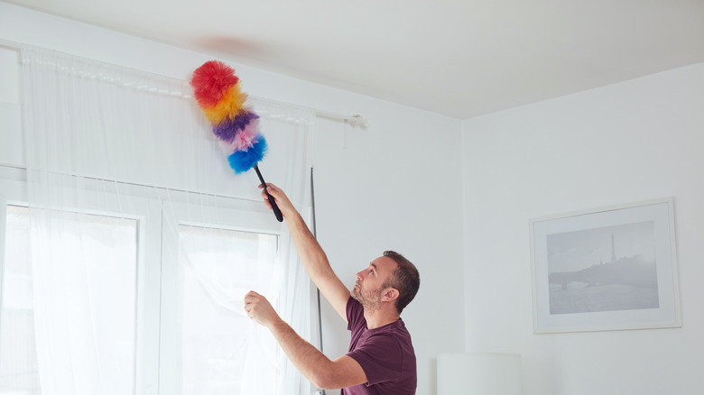 A man dusting off white walls with a colorful duster