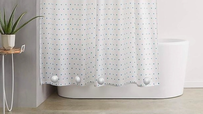 Shower curtain weights hanging on to the bottom of a blue and white curtain in front of a tub