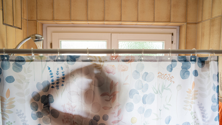 Silhouette of a person in the shower behind a floral shower curtain