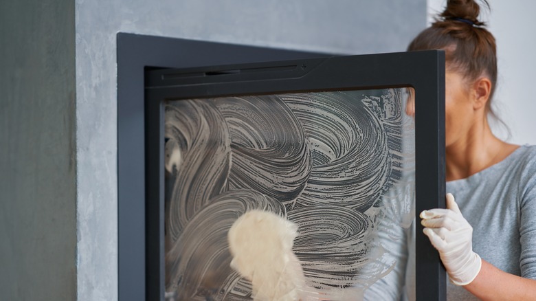 person cleaning fireplace's glass cover