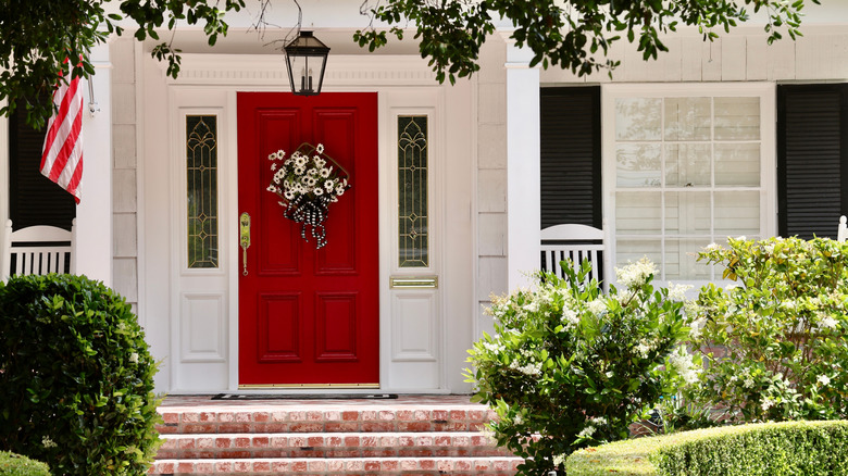 A historic home boasts a vibrant red front door adorned with a floral wreath.