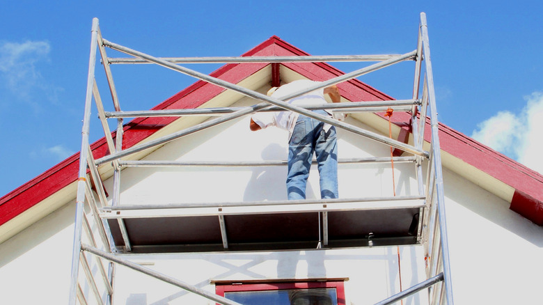 A professional painter paints red accents onto the exterior of a residential house with white walls..