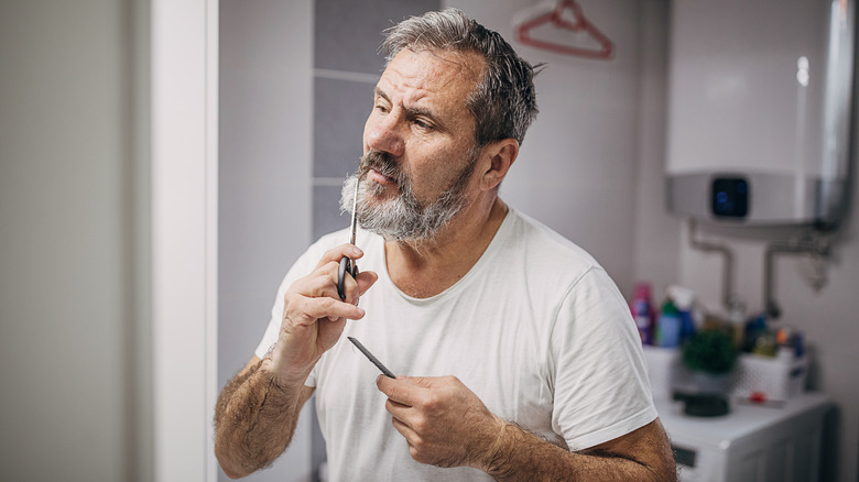 Man trims beard with scissors 