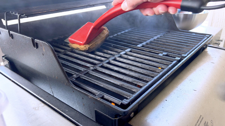 Red brush scrubbing a dirty barbecue grill